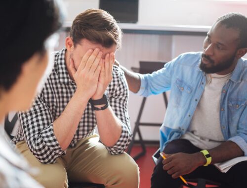 Comforting. Reliable kind black man putting his hand on the shoulder of a crying person while talking to him