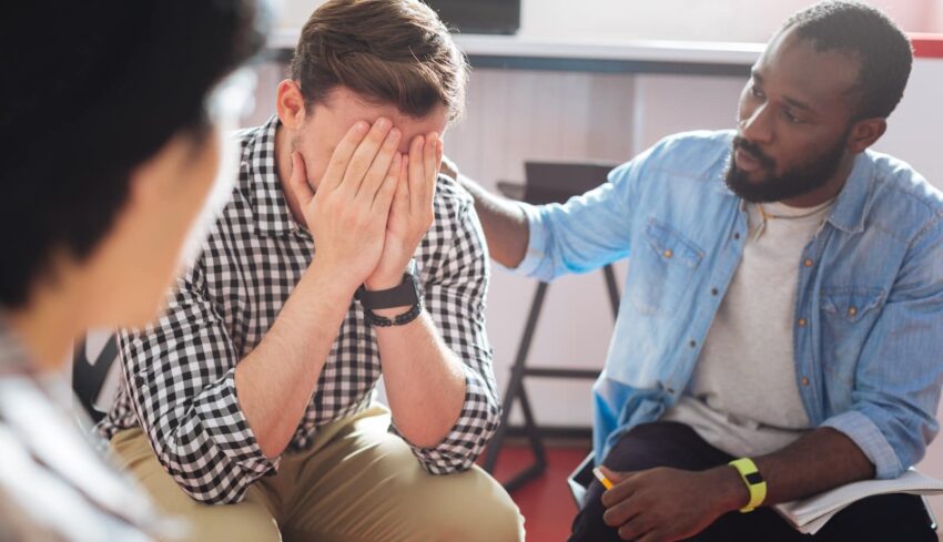 Comforting. Reliable kind black man putting his hand on the shoulder of a crying person while talking to him